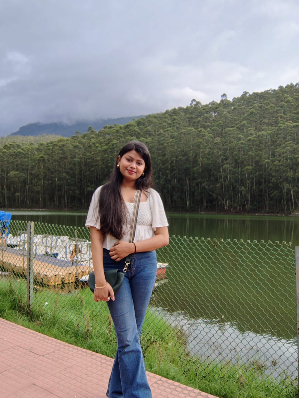 Sanskriti standing by a calm lake surrounded by forested hills in Munnar